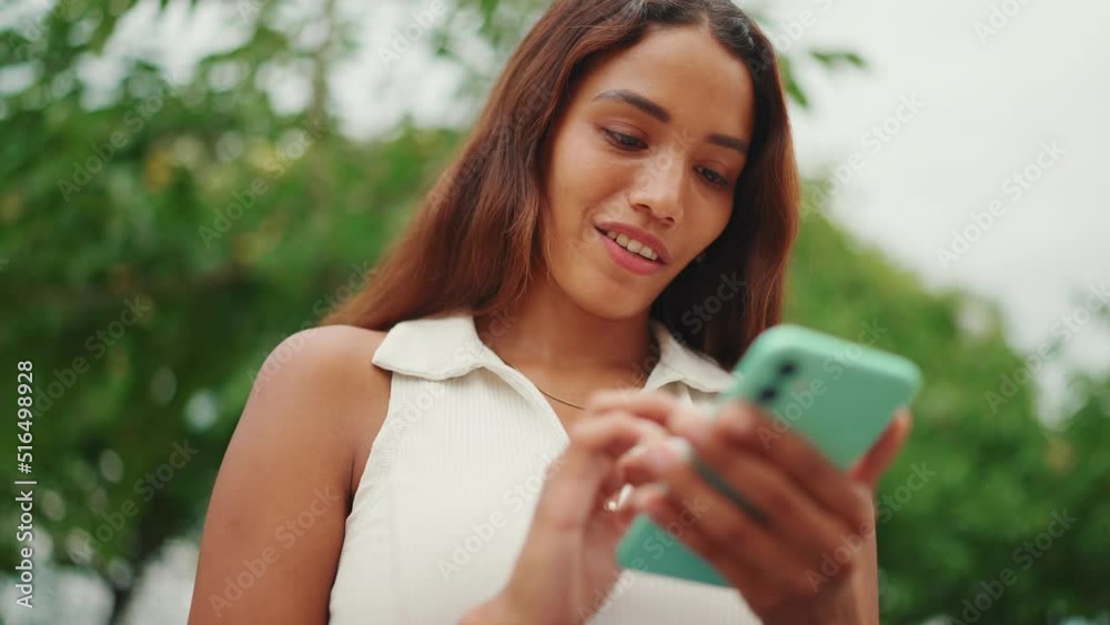 Clouse-up, beautiful girl with long dark hair wearing white top sits on bench and uses mobile phone. Young smiling woman writing in social networks on cellphone. Sideways movement Clouse-up, beautiful girl with long dark hair wearing white top sits on bench and uses mobile phone. Young smiling woman writing in social networks on cellphone. Sideways movement