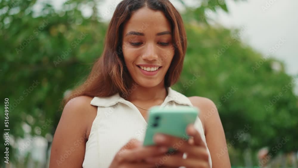 Clouse-up, beautiful girl with long dark hair wearing white top sits on bench and uses mobile phone. Young smiling woman writing in social networks on cellphone. Sideways movement Clouse-up, beautiful girl with long dark hair wearing white top sits on bench and uses mobile phone. Young smiling woman writing in social networks on cellphone. Sideways movement