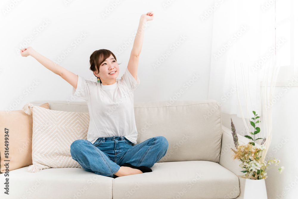 ソファでバンザイしてスッキリ解決した日本人女性（笑顔）
