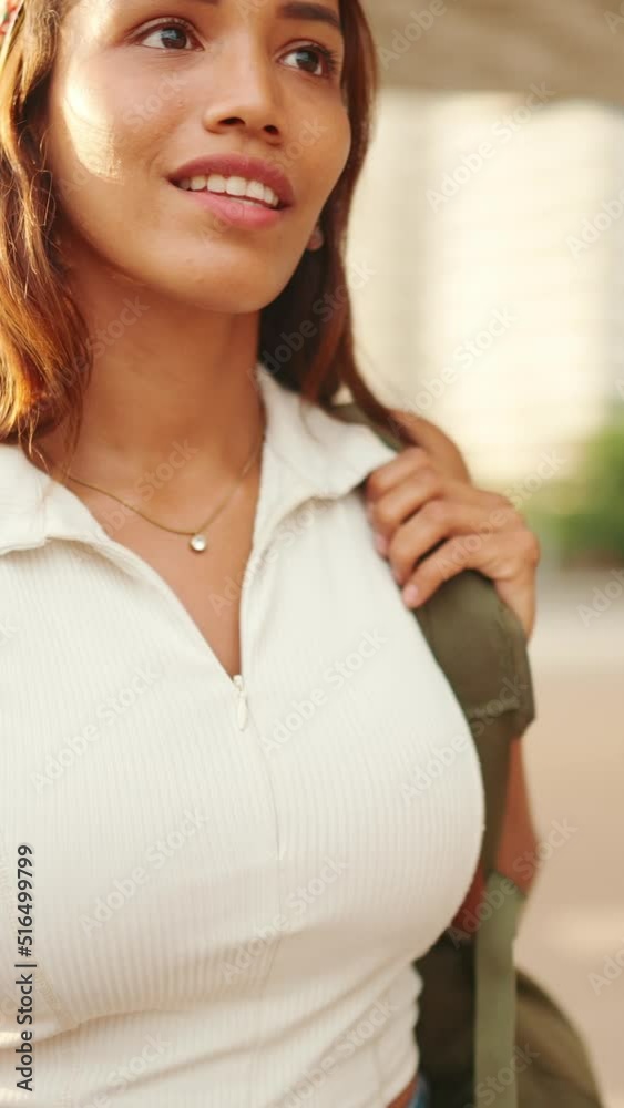 VERTICAL VIDEO: Cute tanned woman wearing white top and yellow bandana with backpack on her shoulder walks down the street. Backlight. Camera moving around