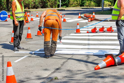 A team of road workers mark a pedestrian crossing on the roadway with white paint.