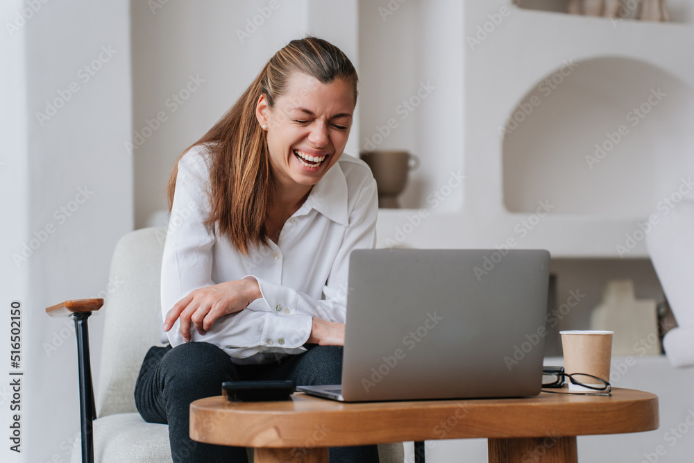 Cheerful hispanic businesswoman sitting at table with laptop laughing eyes closed during video call. Successful manager remote working home. Happy spanish woman enjoying joke of friend while talking. Cheerful hispanic businesswoman sitting at table with laptop laughing eyes closed during video call. Successful manager remote working home. Happy spanish woman enjoying joke of friend while talking.