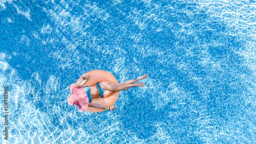 Beautiful woman in hat in swimming pool aerial top view from above, young girl in bikini relaxes and swims on inflatable ring donut and has fun in water on family vacation, tropical holiday resort 