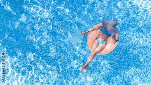 Beautiful woman in hat in swimming pool aerial top view from above, young girl in bikini relaxes and swims on inflatable ring donut and has fun in water on family vacation, tropical holiday resort 