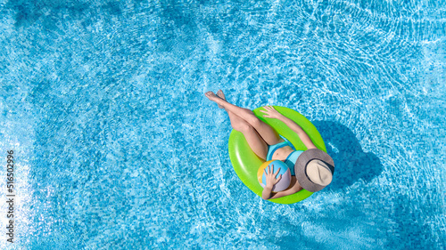 Active young girl in swimming pool aerial drone view from above, teenager relaxes and swims on inflatable ring donut and has fun in water on family vacation, tropical holiday resort 