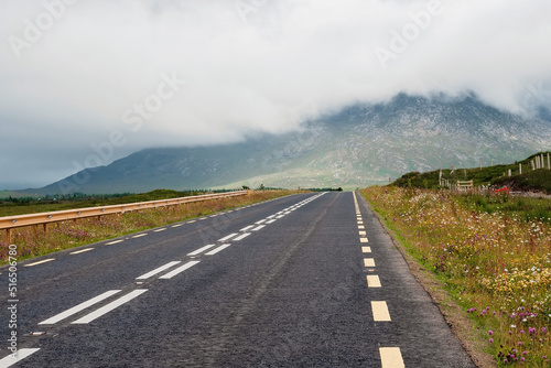 Straight asphalt road to a mountain covered with low clouds. Transportation and tourism. West of Ireland. Calm and peaceful mood.