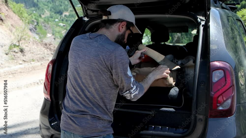 A young man pulls out necessary things from trunk of car, rear view 4k video A young man pulls out necessary things from trunk of car, rear view 4k video