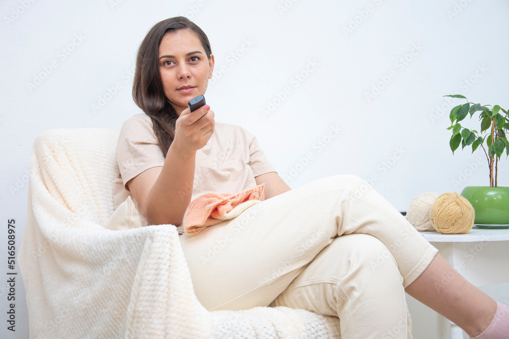 Woman sitting against a white wall holding the remote changes channels Woman sitting against a white wall holding the remote changes channels