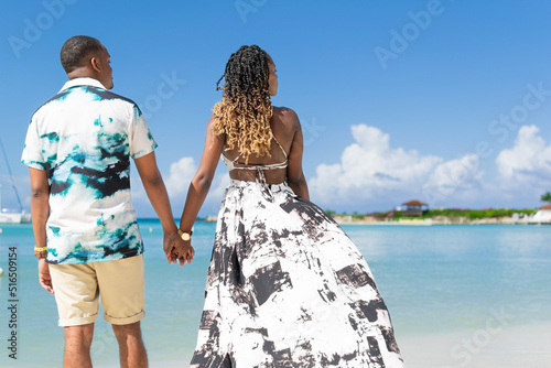 Young black couple holding hands on the beach, photographed from behind. Jamaican couple. 