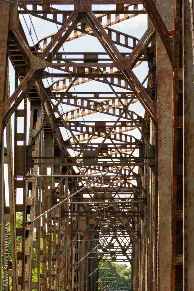 Obraz premium The metal structure of the railway viaduct over the river against the background of a blue sky with clouds.
