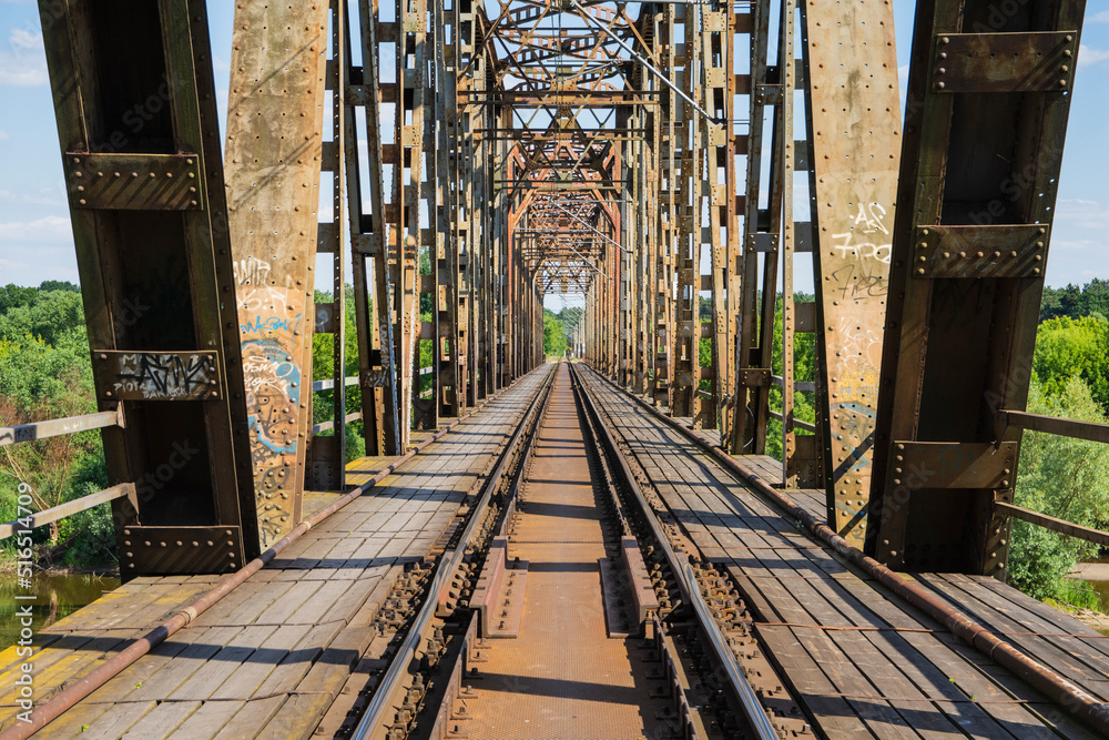 The metal structure of the railway viaduct over the river against the background of a blue sky with clouds. The metal structure of the railway viaduct over the river against the background of a blue sky with clouds.