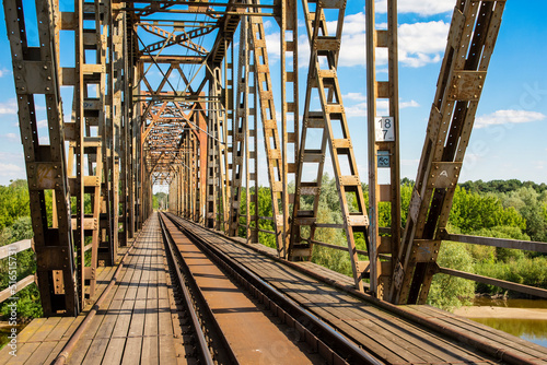 The metal structure of the railway viaduct over the river against the background of a blue sky with clouds.