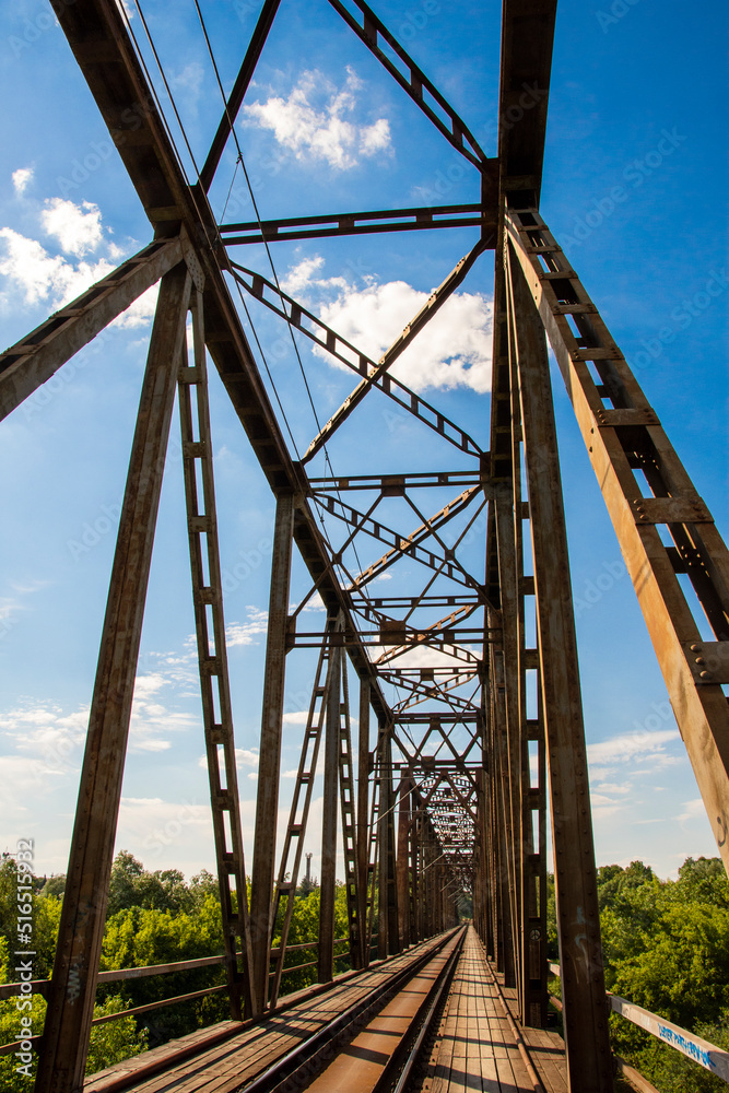 The metal structure of the railway viaduct over the river against the background of a blue sky with clouds. The metal structure of the railway viaduct over the river against the background of a blue sky with clouds.