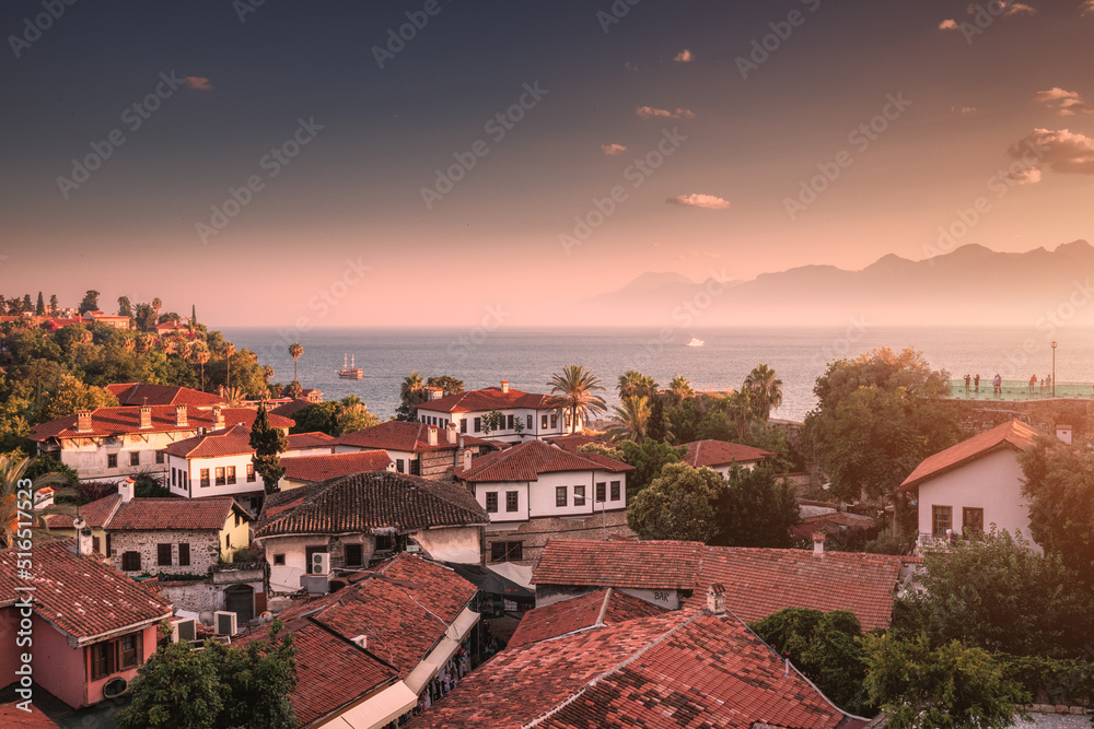Panoramic viewpoint with vistas over red tiled roofs of hotels in Antalya resort old town and blue sea in the background. Majestic sunset clouds and mountains in a haze