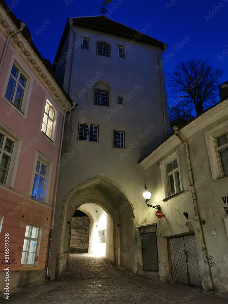 An old house with a through arched passage on one of the narrow streets of Old Tallinn against the blue sky. Spring evening.