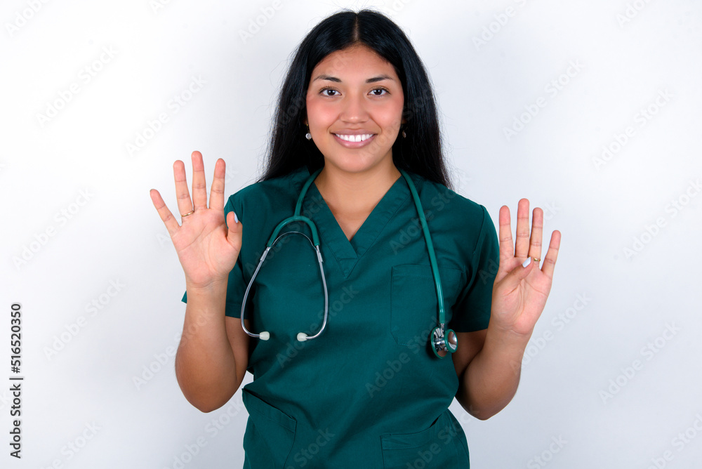 Doctor hispanic woman wearing surgeon uniform over white wall showing and pointing up with fingers number nine while smiling confident and happy. Doctor hispanic woman wearing surgeon uniform over white wall showing and pointing up with fingers number nine while smiling confident and happy.