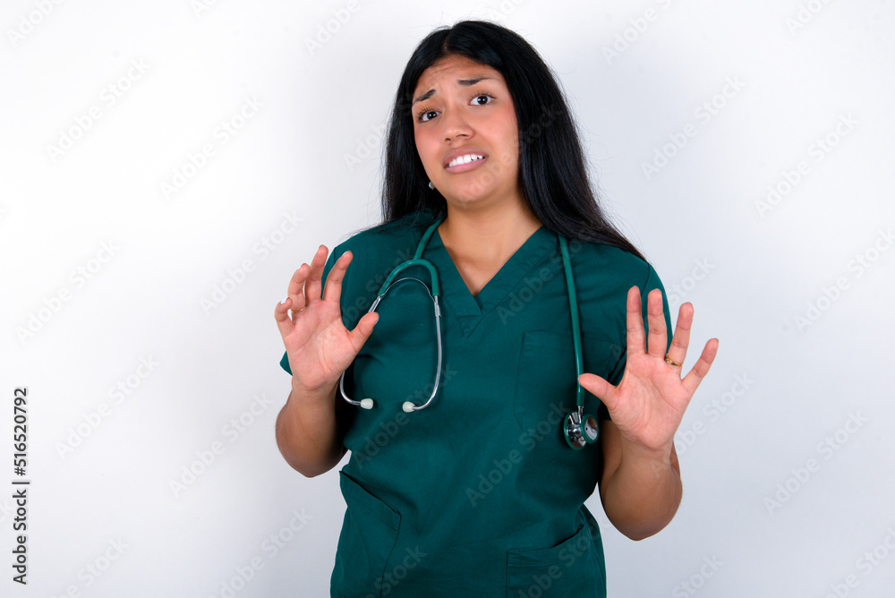 Doctor hispanic woman wearing surgeon uniform over white wall afraid and terrified with fear expression stop gesture with hands, shouting in shock. Panic concept. Doctor hispanic woman wearing surgeon uniform over white wall afraid and terrified with fear expression stop gesture with hands, shouting in shock. Panic concept.