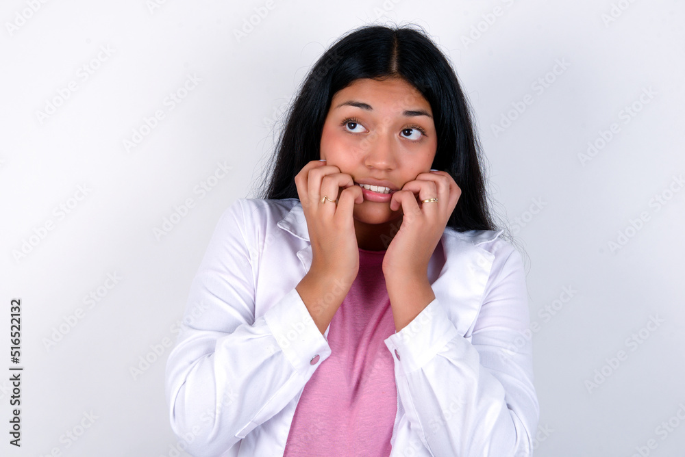 Terrified Young hispanic doctor girl wearing coat over white background looks empty space home alone moonless night Terrified Young hispanic doctor girl wearing coat over white background looks empty space home alone moonless night