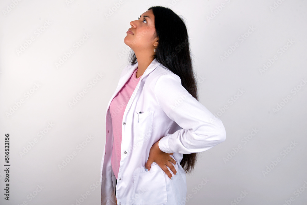 Young hispanic doctor girl wearing coat over white background got back pain Young hispanic doctor girl wearing coat over white background got back pain