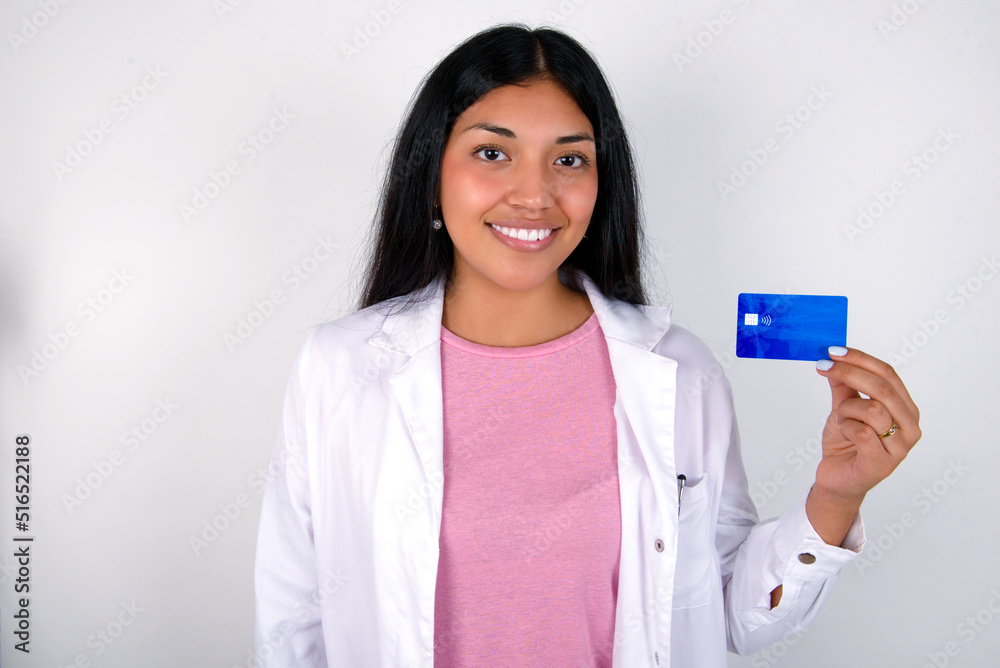 Photo of happy cheerful smiling positive Young hispanic doctor girl wearing coat over white background recommend credit card Photo of happy cheerful smiling positive Young hispanic doctor girl wearing coat over white background recommend credit card