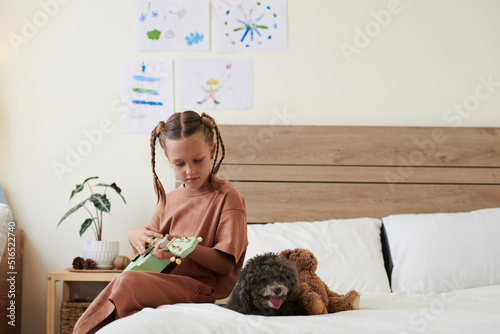 Preteen girl sitting on bed and playing ukulele for her little dog