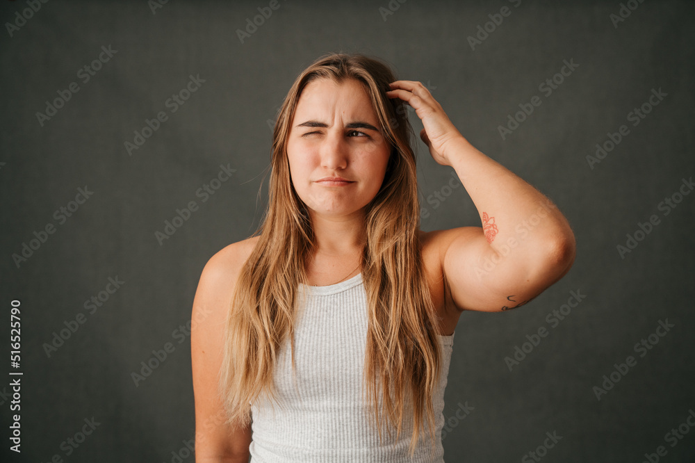 Young blond female scratching her head and thinking