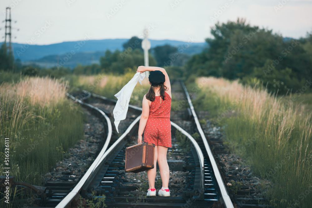 A little girl in a dress walking on an abandoned railroad tracks.