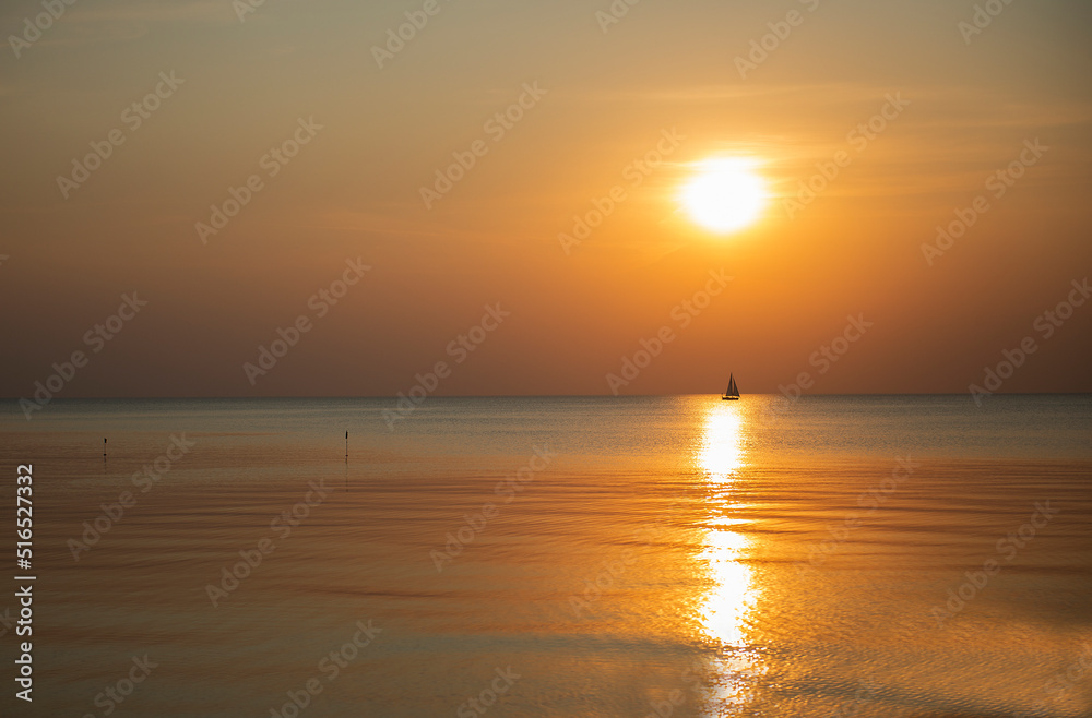 Golden sea and sunset sky with the silhouette of a small sailboat on the horizon