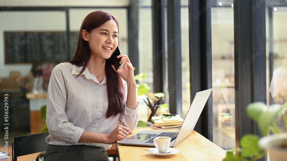 Successful young asian woman investor having phone conversation and using laptop at coffee shop Successful young asian woman investor having phone conversation and using laptop at coffee shop