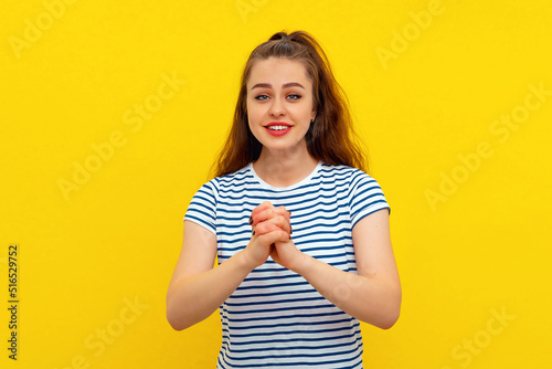Hopeful brunette girl in white-blue striped t shirt wishing to have something, daydreaming, pleading to achieve something, standing hopeful over yellow background