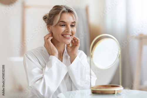 Cheerful beautiful adult lady using hydrating face cream photo