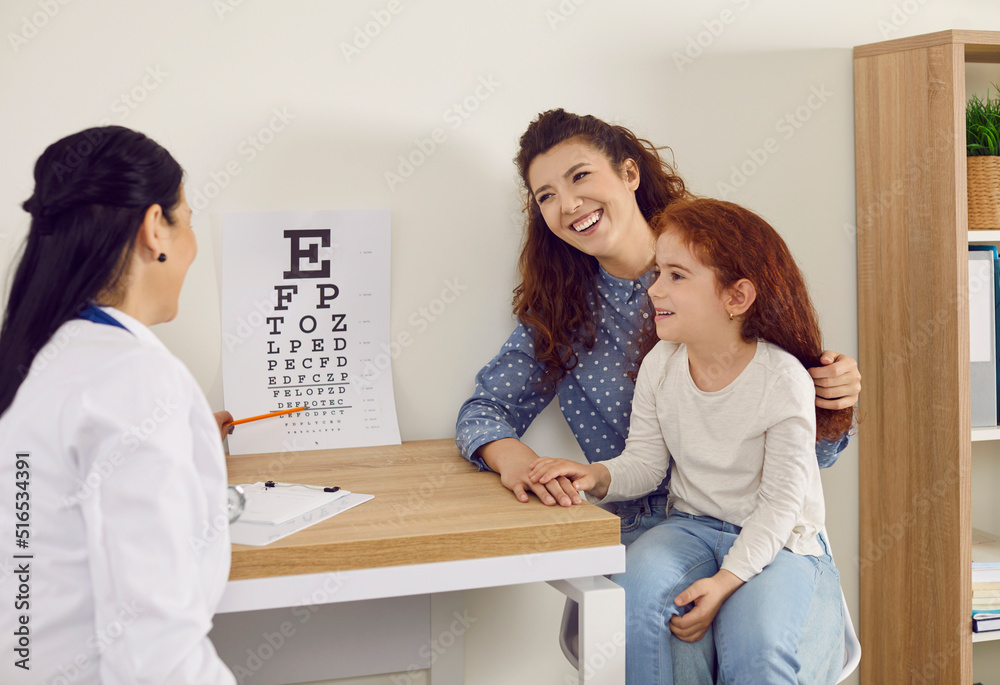 Joyful mother and her little cute daughter at reception in office of female pediatric ophthalmologist. Doctor points to letters on chart for vision test during medical examination and consultation. Joyful mother and her little cute daughter at reception in office of female pediatric ophthalmologist. Doctor points to letters on chart for vision test during medical examination and consultation.