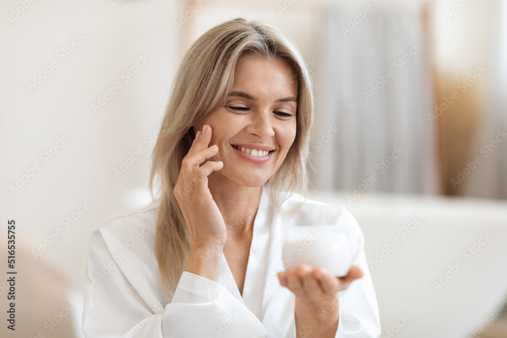 Positive blonde woman using luxury facial cream Positive blonde woman using luxury facial cream