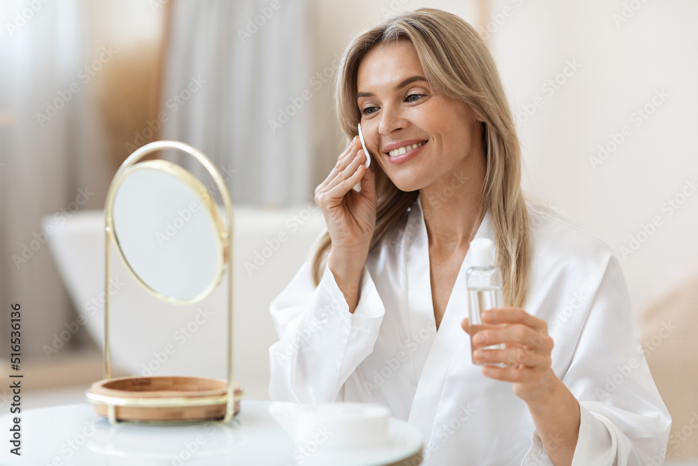 Attractive blonde woman using face tonner, looking at mirror Attractive blonde woman using face tonner, looking at mirror