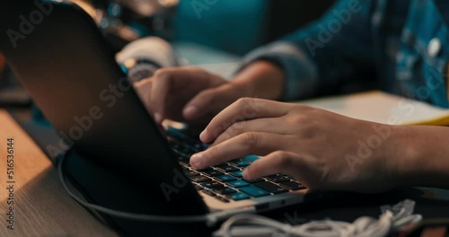Close-up of girl's hands taking notes with pencil in notebook, laptop, headphones, teenage girl has remote lessons, distance learning, online school.