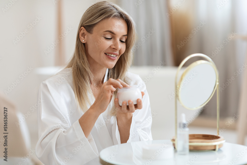 Happy blonde woman applying beauty product on her face