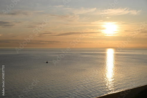 Sun setting over the calm sparkling waters of Port Phillip Bay, with light cloud in the sky, as a small boat heads towards the shore photo