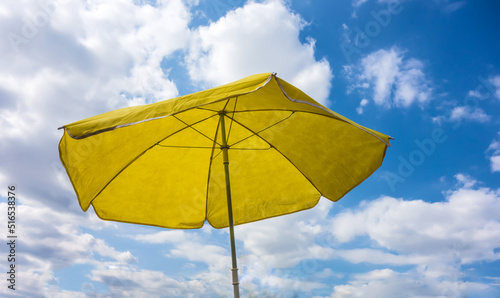 Yellow parasol against summer blue sky with clouds
