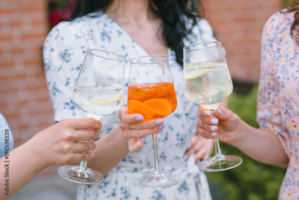 Girls holding cocktails, clinking glasses. Friends enjoying summer in the city.