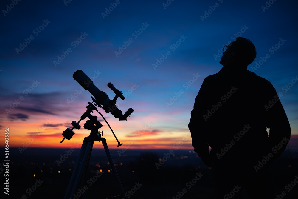 Silhouette of a man, telescope and countryside under the starry