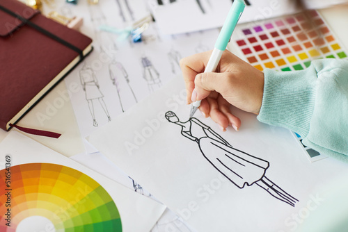 Close-up of unrecognizable female designer sitting at table with color palettes and sketches and creating design of dress