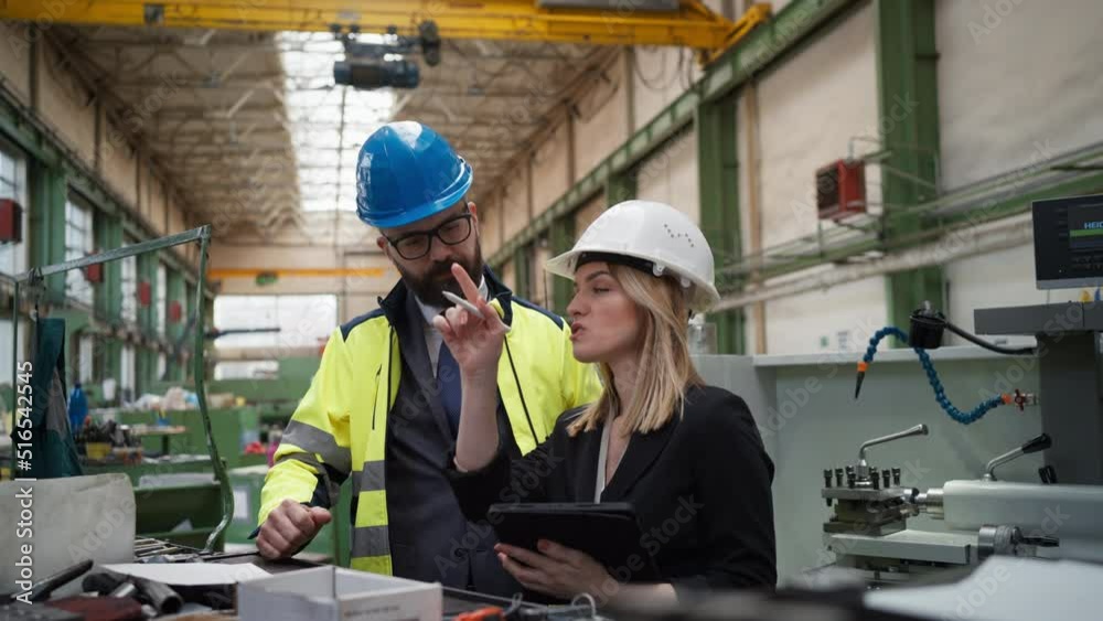 Male and female industrial engineers discussing factory's new machinery project and using tablet. Male and female industrial engineers discussing factory's new machinery project and using tablet.