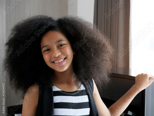 Beautiful african american girl with an afro hairstyle smiling and standing near piano
