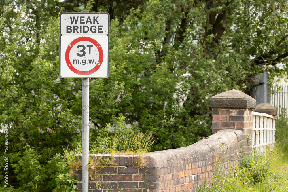 Outdoor white sign on a black pole showing a weak bridge with symbols and numbers Outdoor white sign on a black pole showing a weak bridge with symbols and numbers