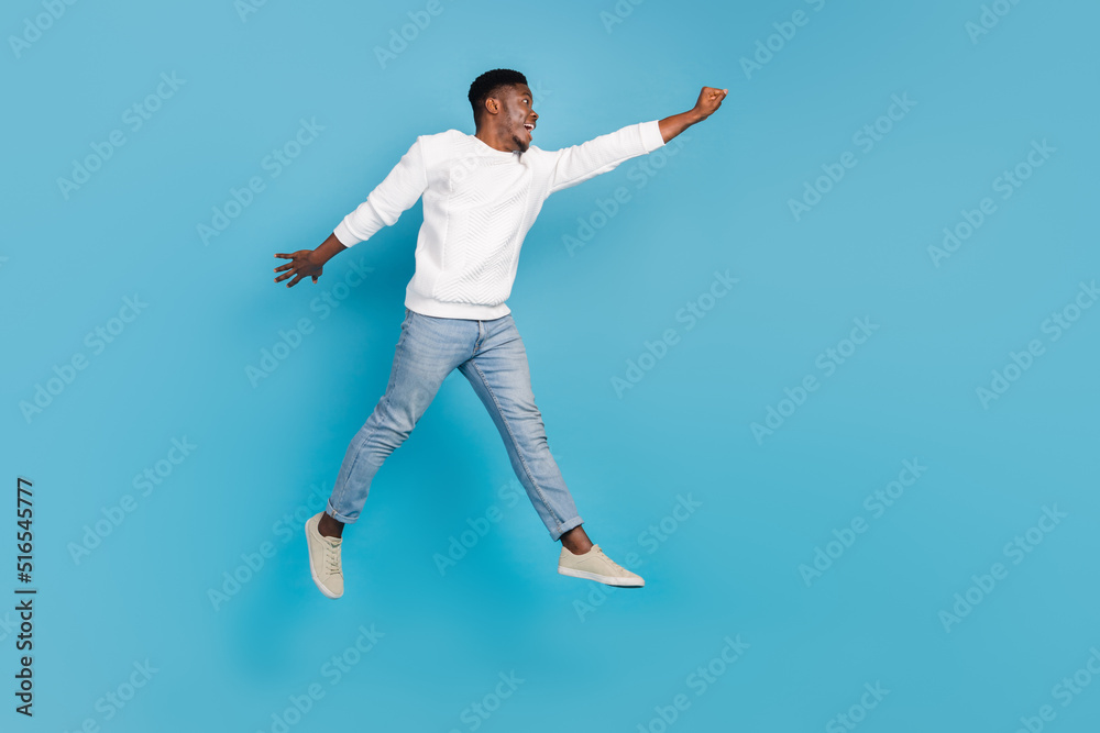 Full size portrait of excited energetic man flight raise arm look empty space isolated on blue color background Full size portrait of excited energetic man flight raise arm look empty space isolated on blue color background