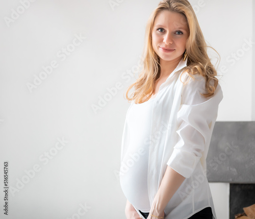 Concept - Young beautiful happy smiling pregnant caucasian blonde girl standing in white light living room
