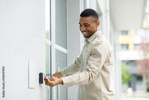 A young man holds an electronic key in front of the entrance door electronic sensor