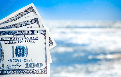 Girl holding money bill of 300 dollars on background of sea ocean waves and blue sky close-up. Hand wave sea ocean money dollars vacation. Concept finance money holiday traveling photo