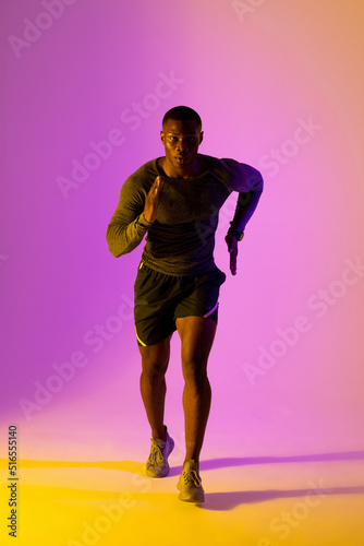 Portrait of african american male runner with sportswear over pink lighting