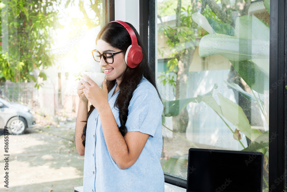 Asian woman with eyeglass listening to music with headphones and holding a cup of coffee
